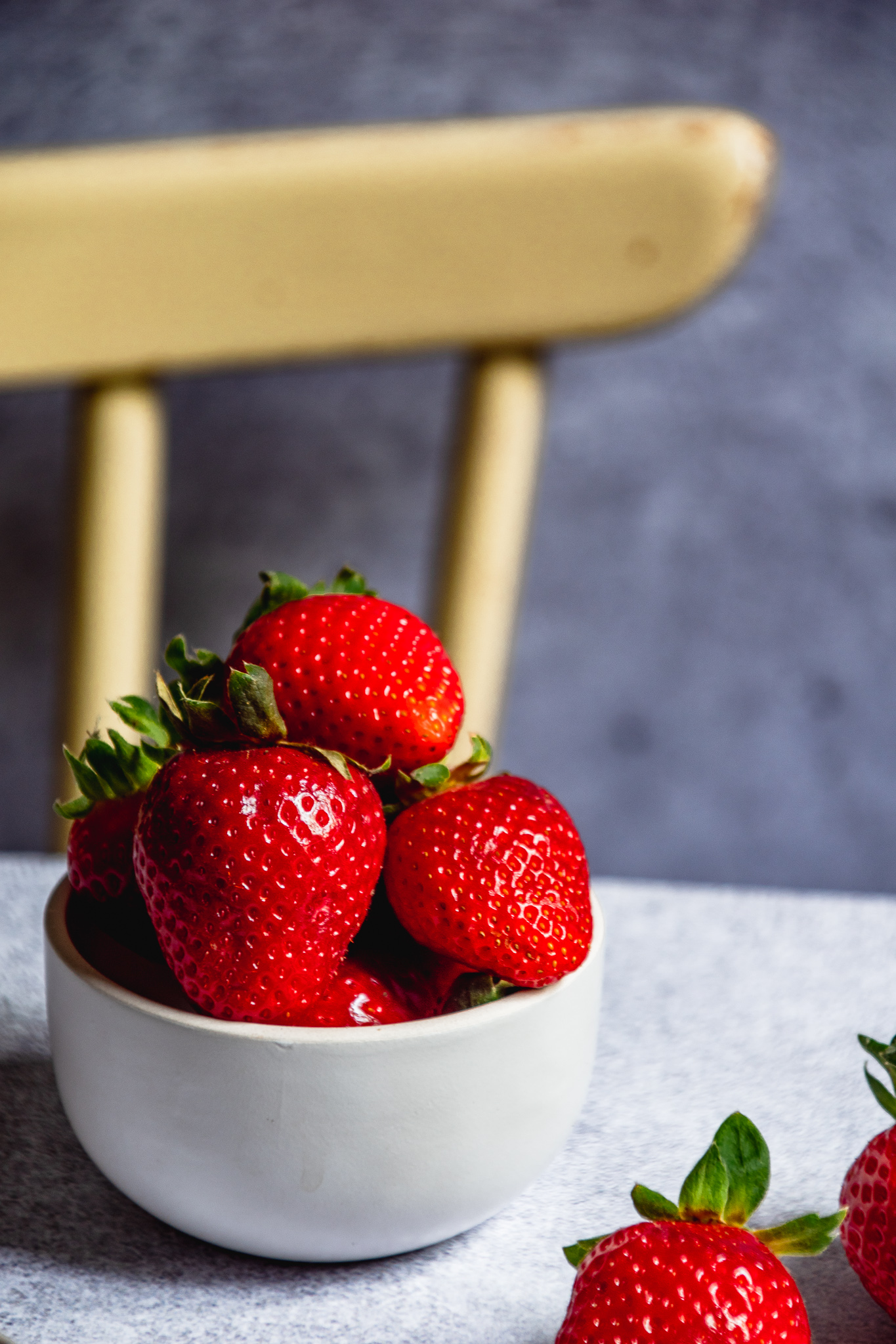 Erdbeeren in einer weißen Schale vor einem beigen Stuhl